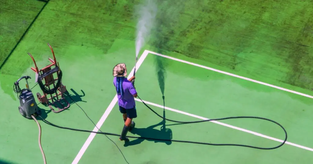 person power washing a tennis court